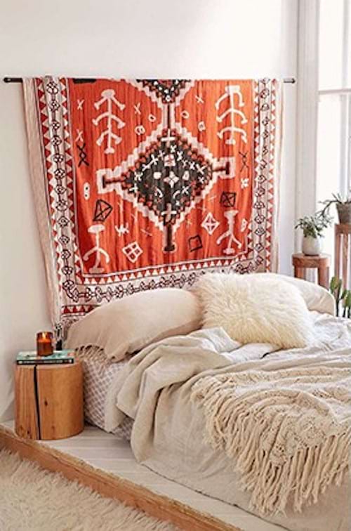 Une tenture orange avec des motifs qui est accrochée au mur et qui forme de tête de lit