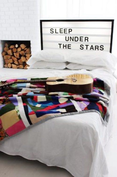Une guitare sur un lit avec une couette de multiples couleurs avec des bûches sur le côté du lit