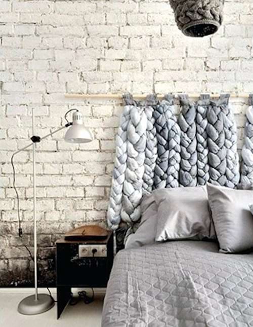 Un lit gris avec une tête de lit en tricot gris et une lampe à proximité du lit