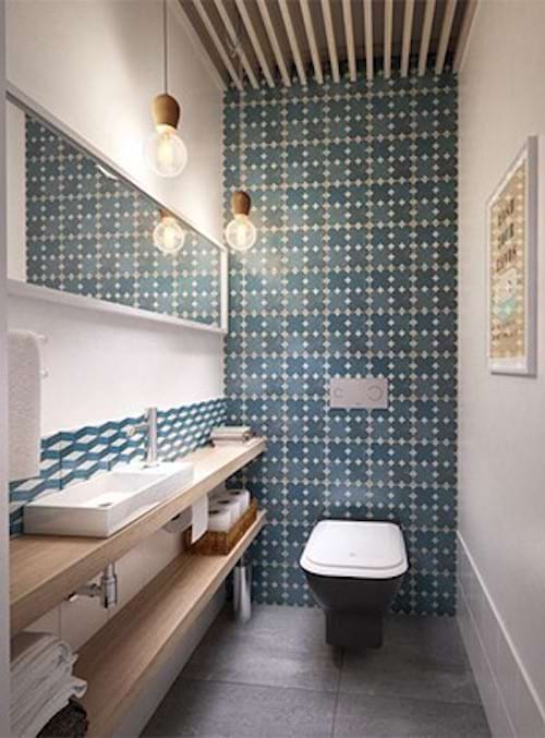 A toilet with a square turquoise wall with a large horizontal mirror and sinks 