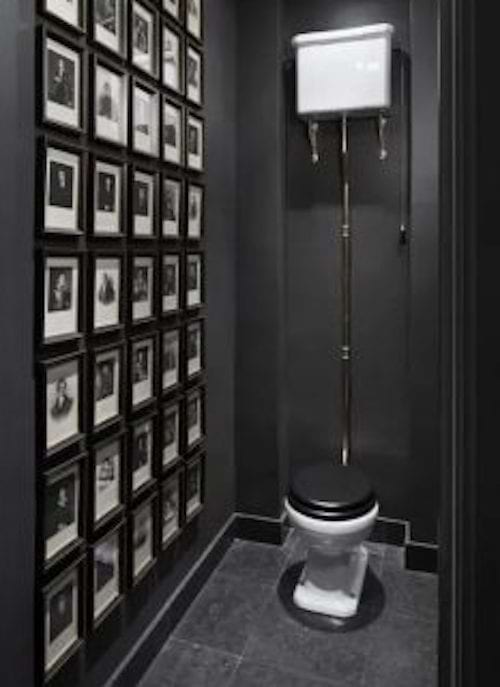 All black toilets with lots of small photo frames hanging on the wall 