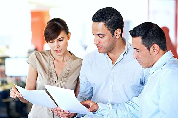 Trois personnes qui regardent chacun deux feuilles qu'ils tiennent