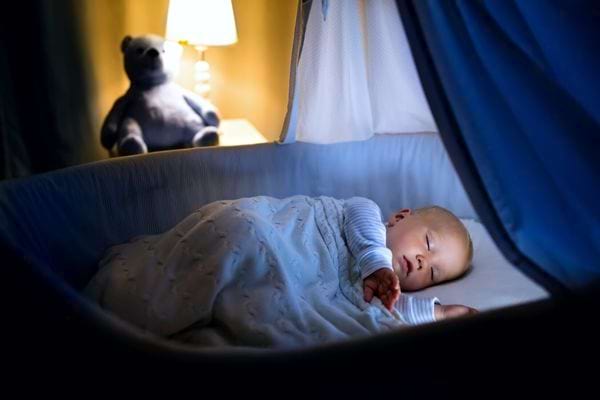 Un bébé qui dort dans son lit la nuit avec sa peluche et une lampe en fond d'image 