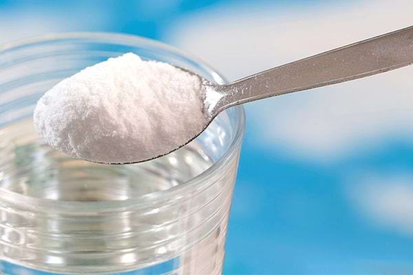 Une cuillère à café de bicarbonate au dessus d'un verre d'eau 