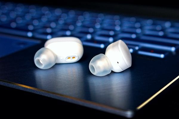 Des écouteurs sans fil blancs posés sur un ordinateur portable