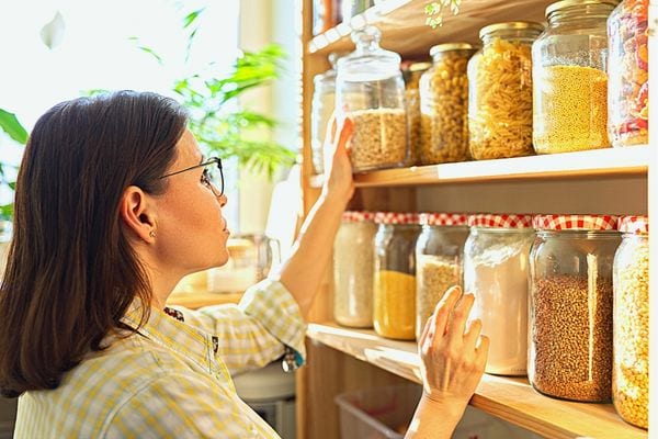 Une femme qui range un bocal en verre remplie d'aliment sur une étagère avec d'autres bocaux 