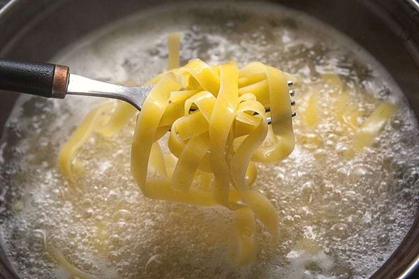 Une fourchette contenant des tagliatelles qui sortent d'une casserole d'eau