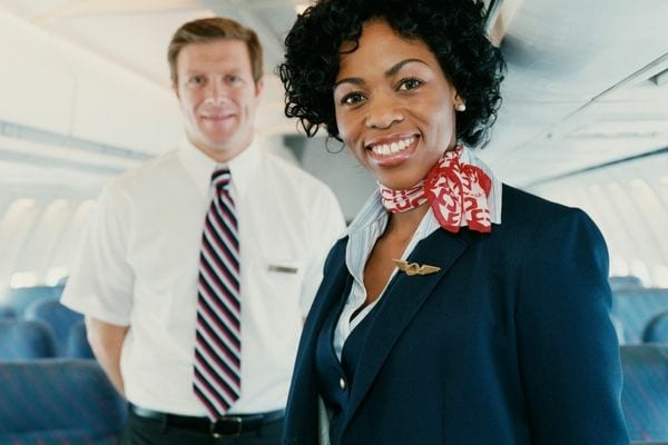 Une hôtesse de l'air noir qui sourit avec un steward juste derrière elle