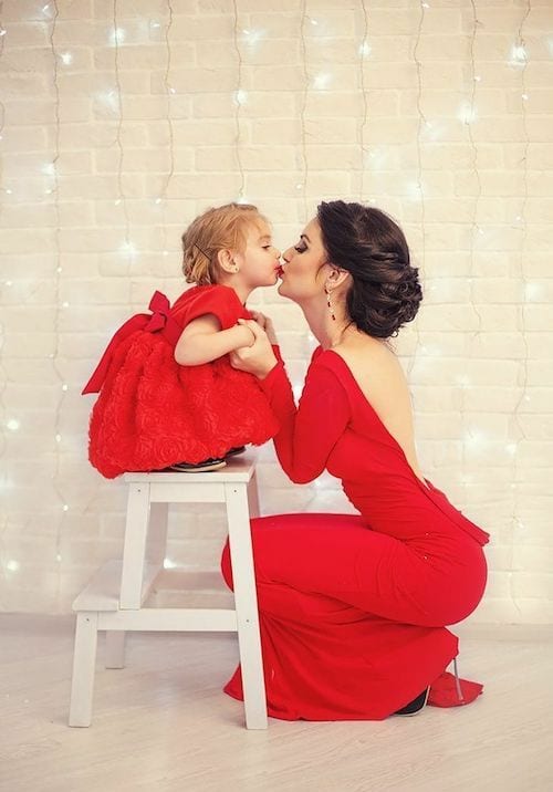 Une maman qui fait un bisous sur la bouche de sa fille qui sont vêtus en robe rouge