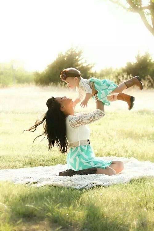 Une mère posée sur un tapis portant sa fille en l'air