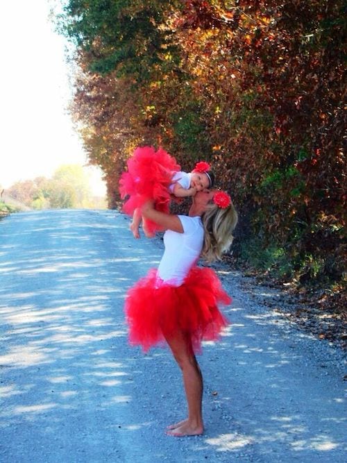 Une maman qui porte sa petite fille en lui faisant un bisous avec des petites tuniques rouge