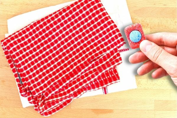 Une personne tenant une pastille de lave-vaisselle avec plusieurs torchons blancs et rouges