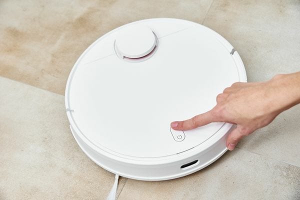 Une personne appuyant sur le bouton d'un aspirateur blanc intelligent