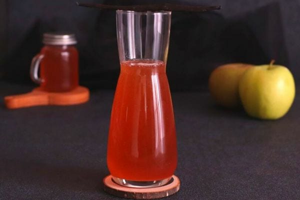 Sciroppo di buccia di la rossa in einem bicchiere alto con due mele the verdi weiter entfernt