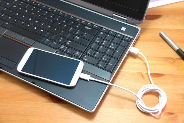 Un smartphone branché via un câble usb sur un ordinateur pour se recharger sans électricité