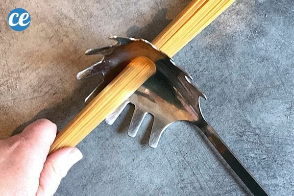 Une personne tenant plusieurs spaghettis qui sont introduites dans le trou d'une cuillère