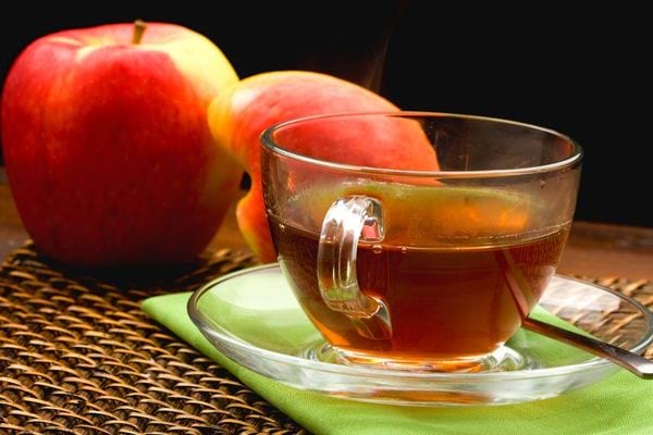 Tisana alla mela con due mele vicino al bicchiere di tisana sur un piattino