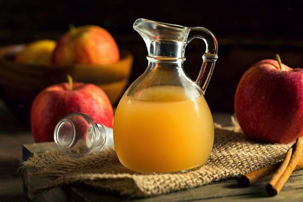 Une carafe en verre avec du vinaigre de cidre et plusieurs pommes tout autour
