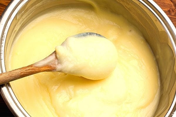Une grosse casserole avec une cuillère en bois contenant de la crème patissière