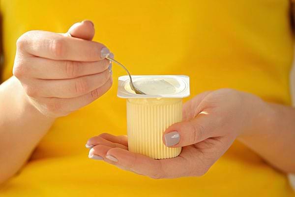 Une femme qui a un tee-shirt jaune et qui mange un petit suisse