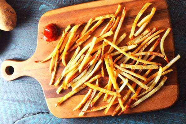 Plusieurs frites sur une planche à découper en bois avec du ketchup