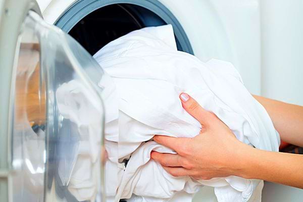 Une femme qui tient un linge blanc devant une machine à laver