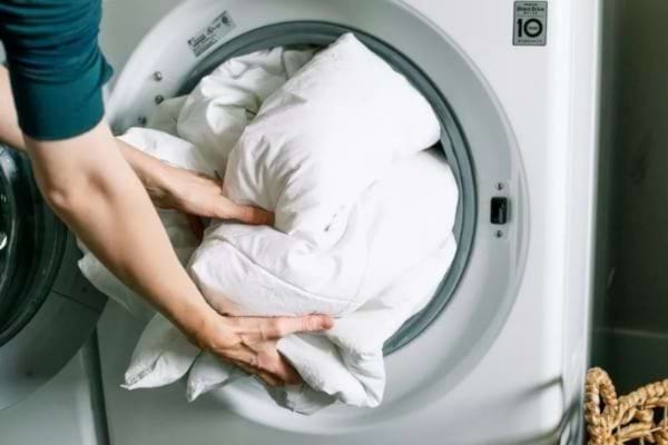 Une personne qui mets du linge blanc dans le tambour d'une machine à laver 
