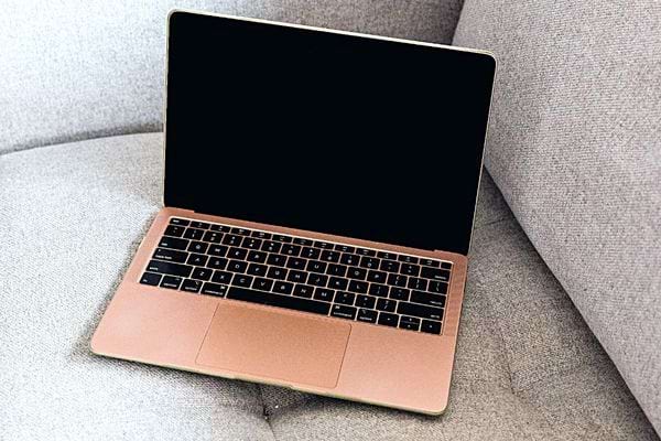 Un MacBook Air rose ouvert et en veille sur un canapé gris