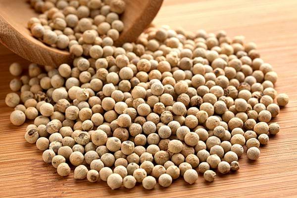 Plusieurs gros grains de poivre blancs sur une table en bois