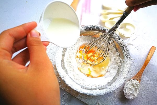Une personne rajoutant un liquide blanc dans une pâte à gateau en préparation dans un bol