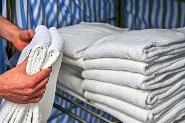 Une personne qui tient deux serviettes blanches à côté de plusieurs piles de serviettes blanches