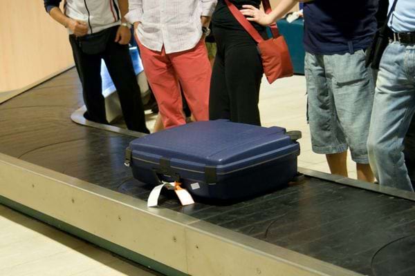 Plusieurs personnes à l'aéroport devant une valise bleue 