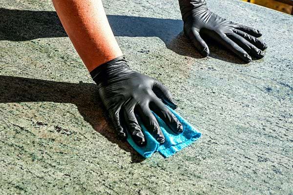 Une personne avec des gants en latex noirs qui désinfecte du marbre