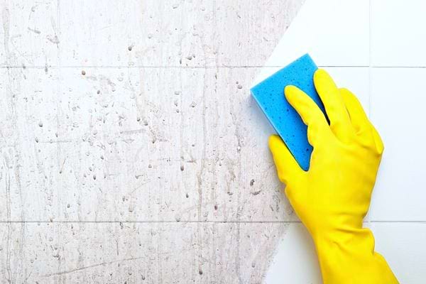 Une personne avec un gant en latex jaune qui nettoie un mur sale 