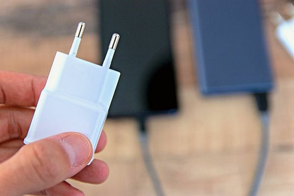 Une personne qu tient un chargeur blanc au dessus d'un smartphone en arrière-plan 