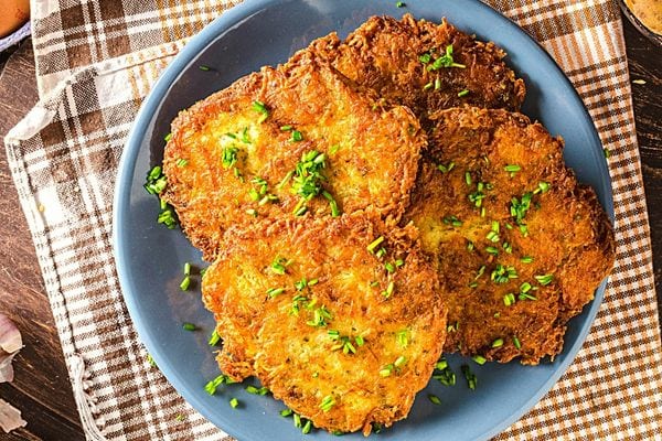Une assiette grise remplie de galettes de pommes de terre avec quelques herbes aromatiques