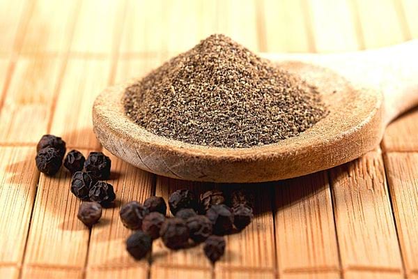 Du poivre en poudre dans une spatule en bois avec des gros grains à côté