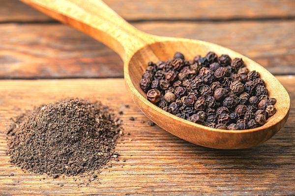 Des gros grains de poivre dans une cuillère en bois avec du poivre en poudre
