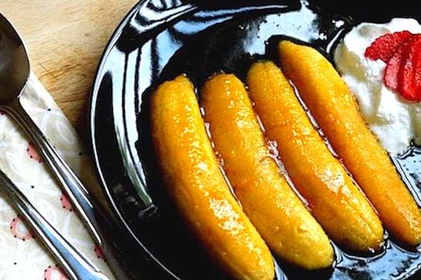 Vier mit Rum und Orange flambierte Bananen auf einem schwarzen Teller