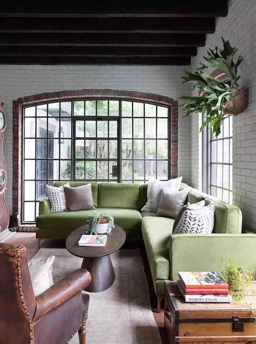 Um grande sofá de canto verde com janelas envidraçadas atrás dele