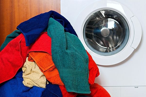 Plusieurs serviettes de multiples couleurs devant une machine à laver