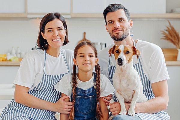 Une mère et un père portant un tablier bleu et blanc avec leur fille et un chien 