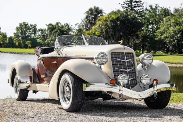 Une voiture ancienne avec des pneus noirs et blancs devant un lac