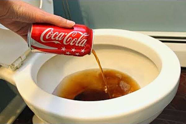 Une personne versant une canette de Coca-Cola dans des toilettes 