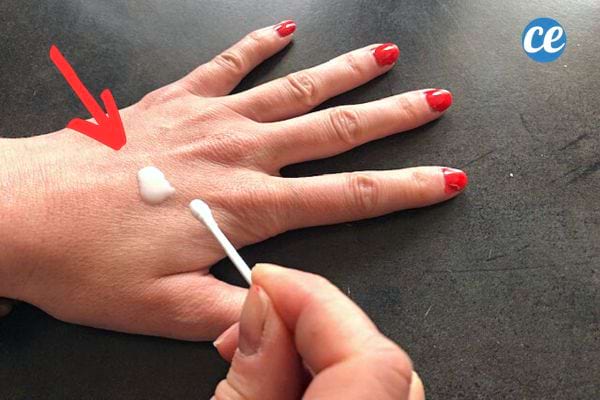 Une femme tenant un coton-tige avec de la crème sur sa main et du vernis sur ses ongles 