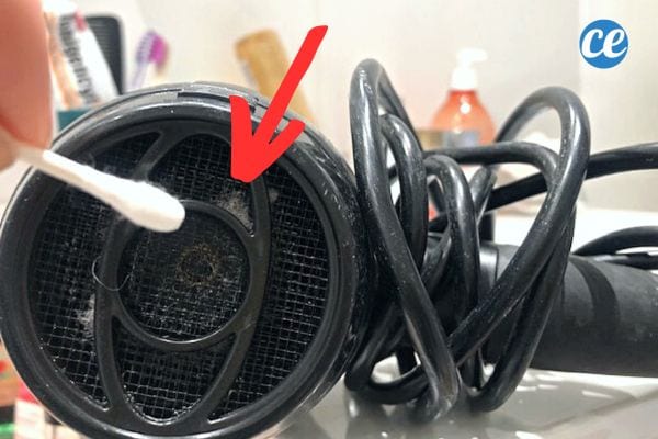 Une personne tenant un coton-tige devant le ventilateur d'un sèche-cheveux noir 