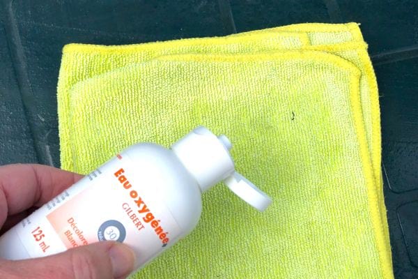 Une personne mettant de l'eau oxygénée sur un chiffon micro-fibre jaune