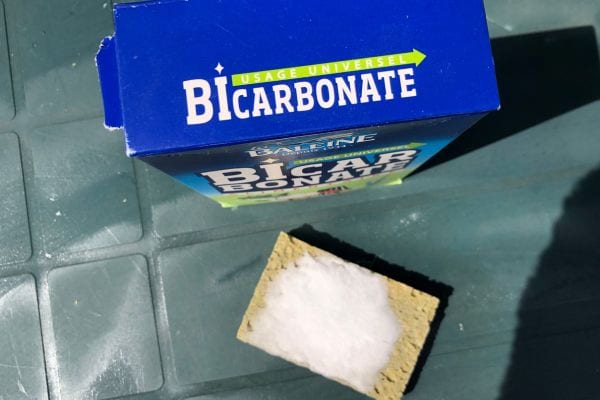 Un paquet bleu de bicarbonate de soude avec une éponge jaune sur une table verte