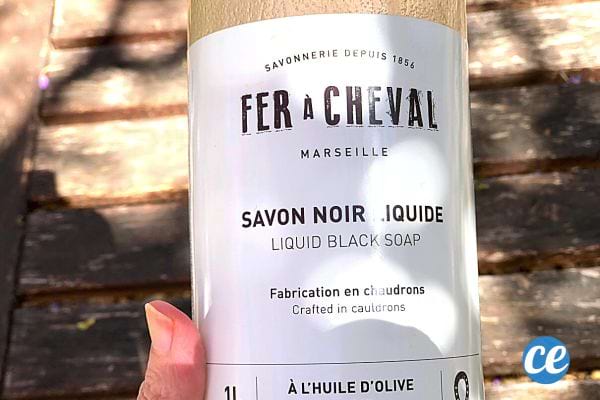Une femme tenant une bouteille de savon noir liquide fer à cheval 