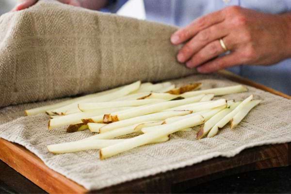 Une personne qui sèche plusieurs frites à l'aide d'un torchon 